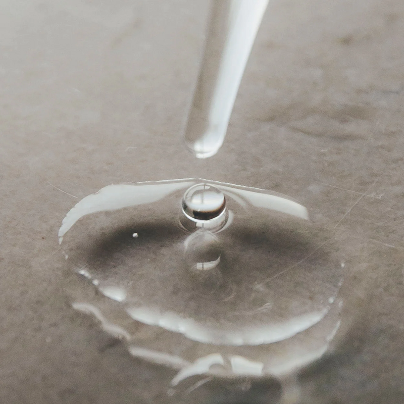 Close-up of a water droplet on a surface with a clear dropper above.