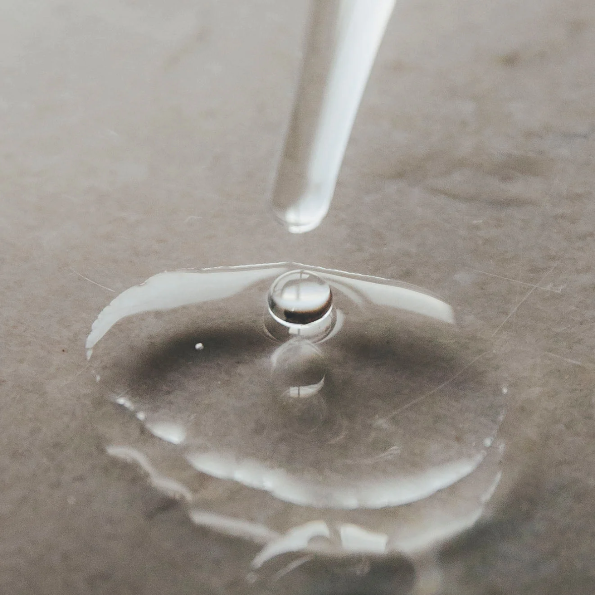 Close-up of a water droplet on a surface with a clear dropper above.